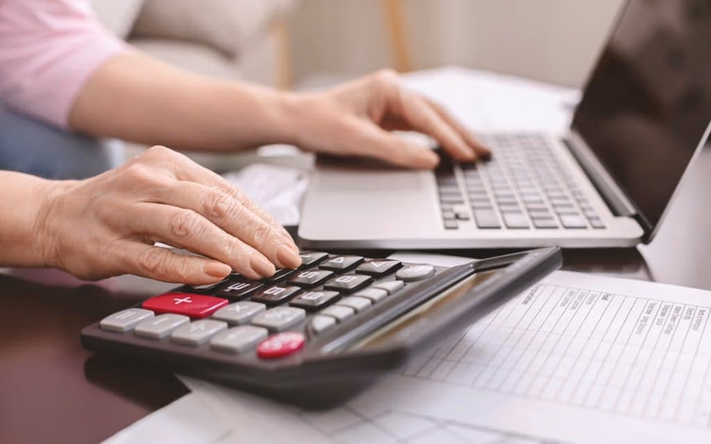 Senior woman with calculator counting dollar money at home